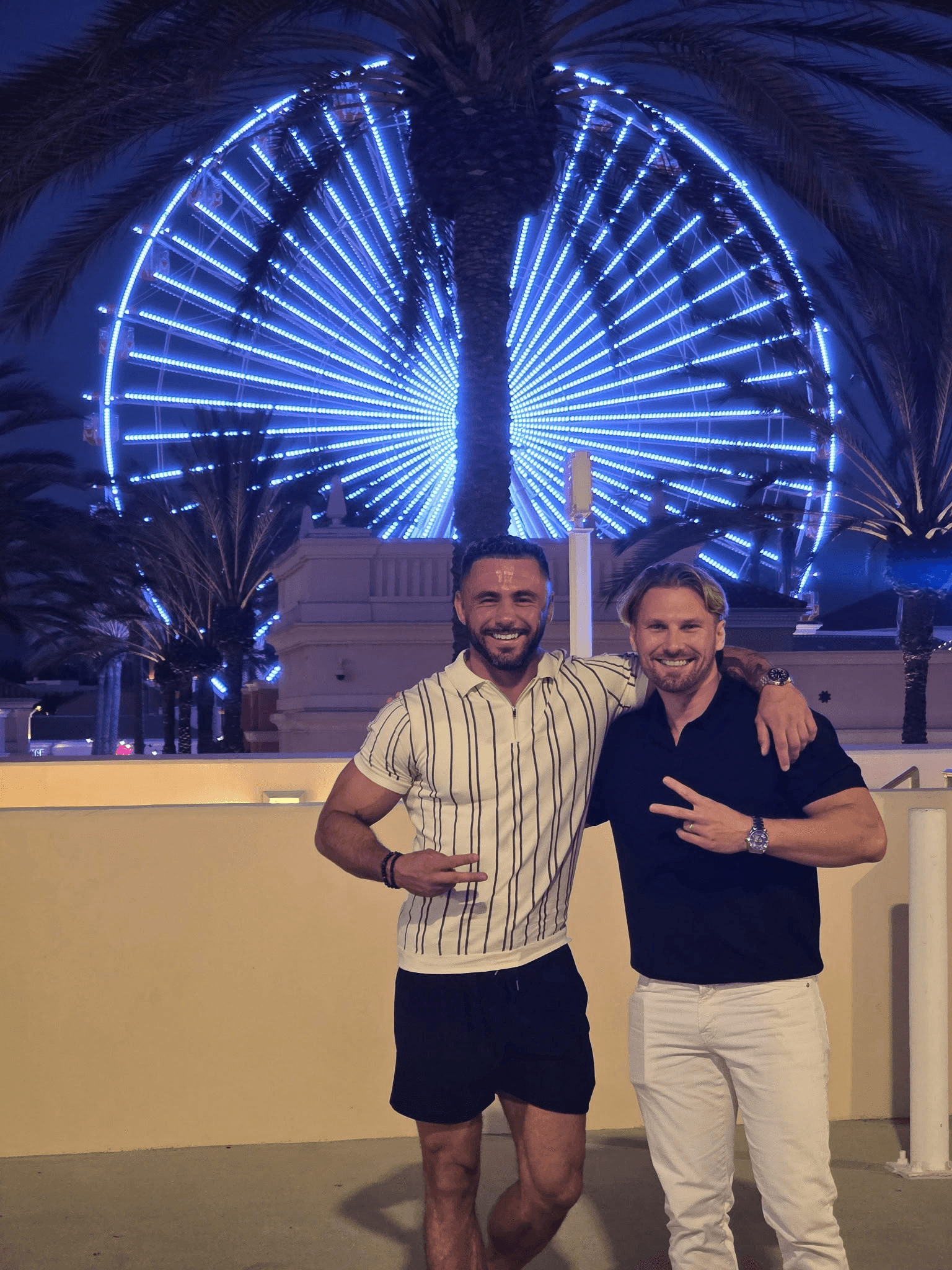 Gabby’s Home Services owners Pawel Parda and Daniel Zajac together beneath a palm and an illuminated Ferris wheel.